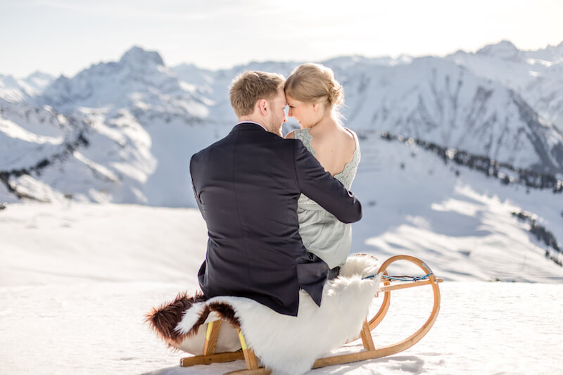 Hochzeitspaar sitzt auf Schlitten im Gebirge
