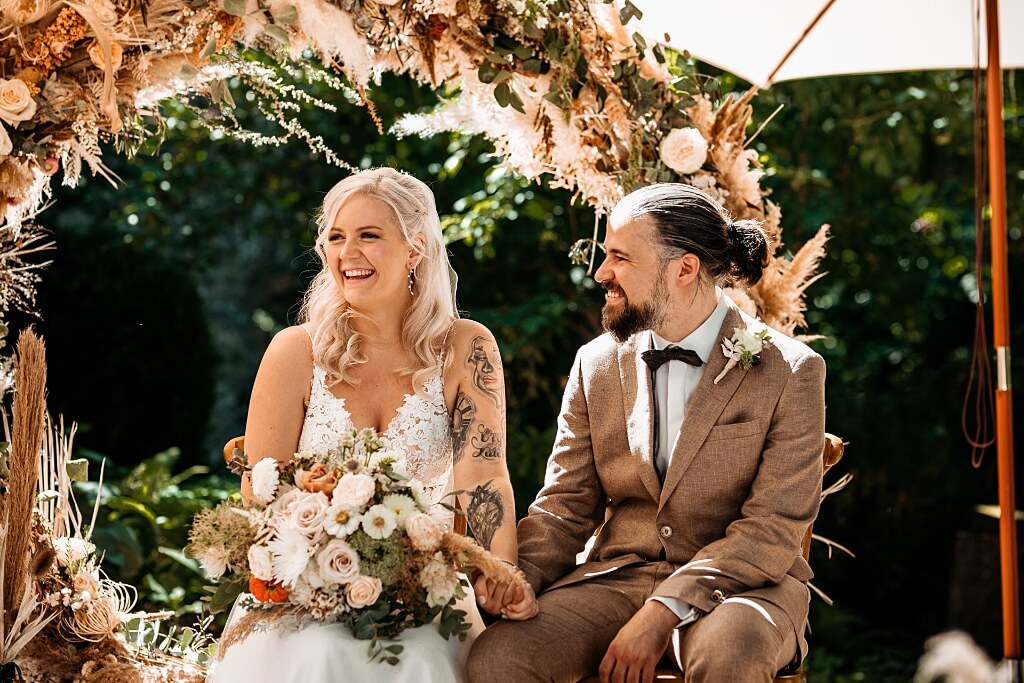 Hochzeit planen | Hochzeitspaar sitzt unter Blumenbogen