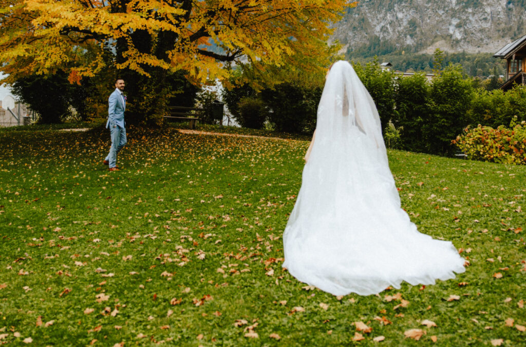 Ein Mann steht im Garten und schaut auf eine Braut in einem weißen Kleid, die im Freien für eine Hochzeitszeremonie vorbereitet wird.