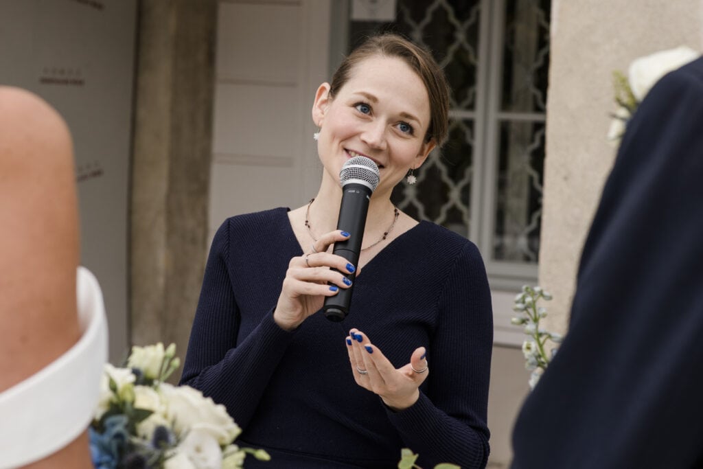 Sprecherin bei Trauung mit Mikrofon bei Freie Redner Österreich, Porträt einer jungen Frau, die bei einer Hochzeitsrede spricht, professionell, emotionale Rede, Event, Zeremonie, freie Trauung.