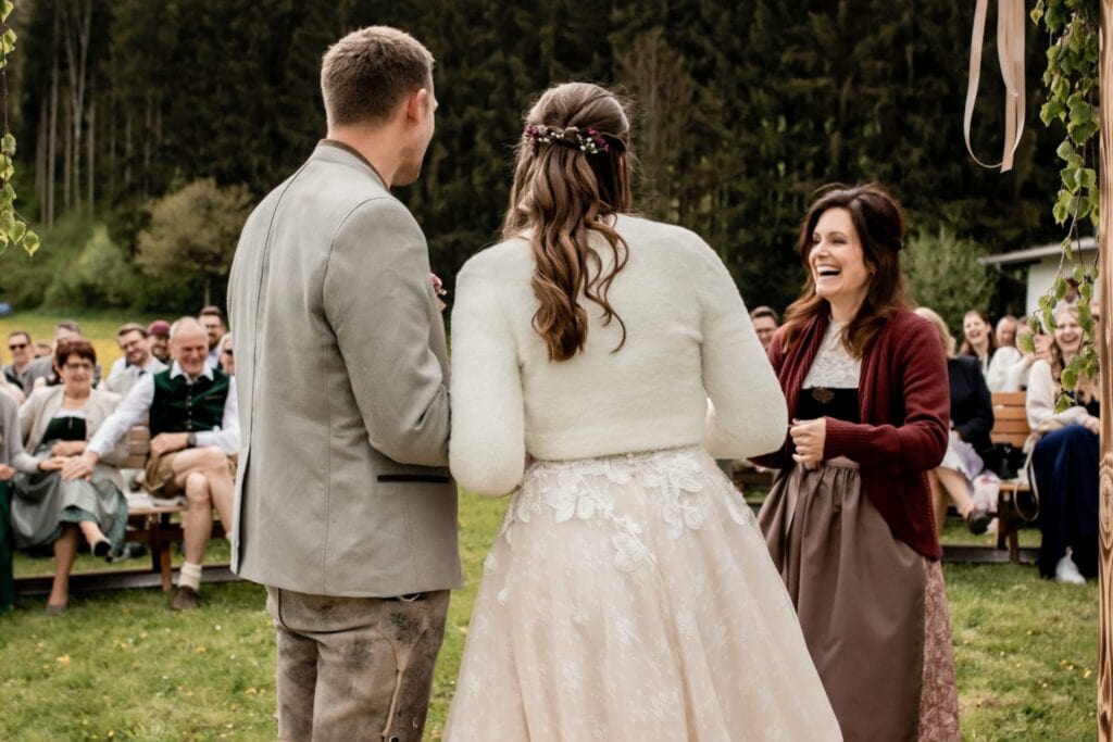 Braut und Bräutigam bei ihrer Trauung im Freien, umgeben von Freunden und Familie in einer malerischen Naturkulisse in Österreich.