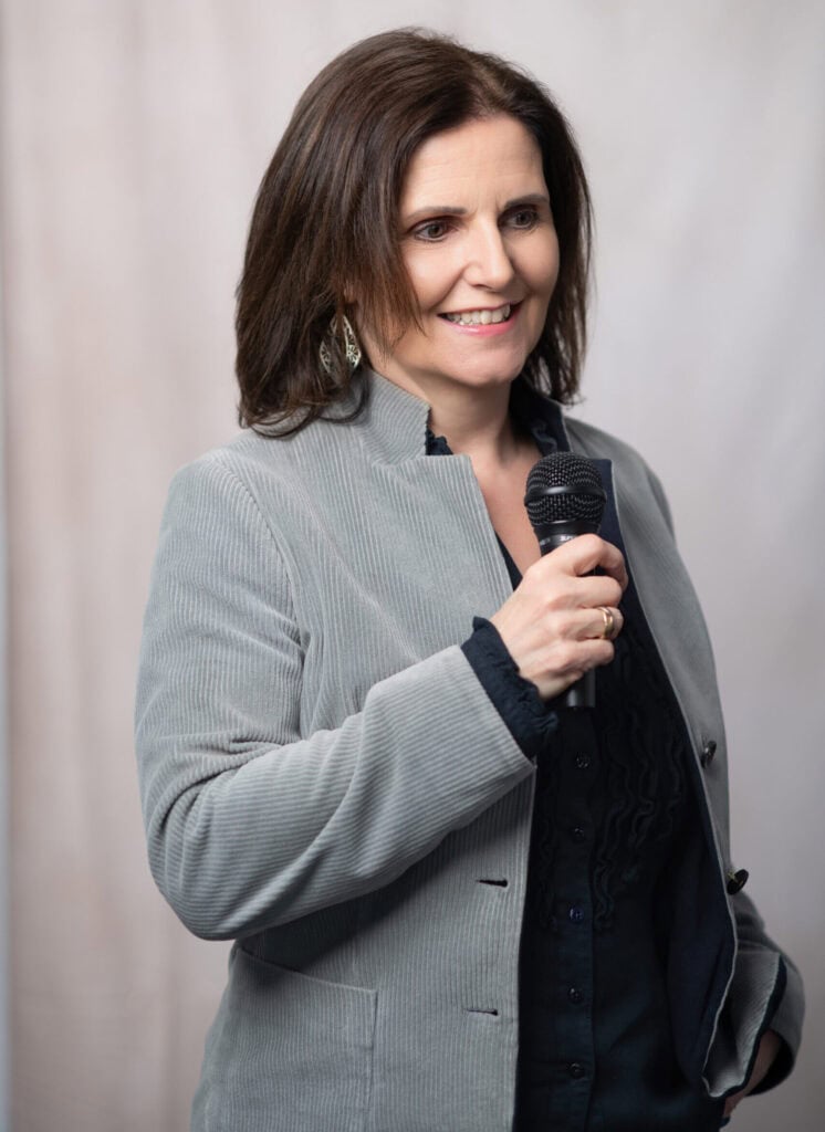 Maria Reingruber hält Mikrofon bei einer Rede, professionell gekleidet, bei einer öffentlichen Veranstaltung in Österreich, Fokus auf Rednerin und Engagement.