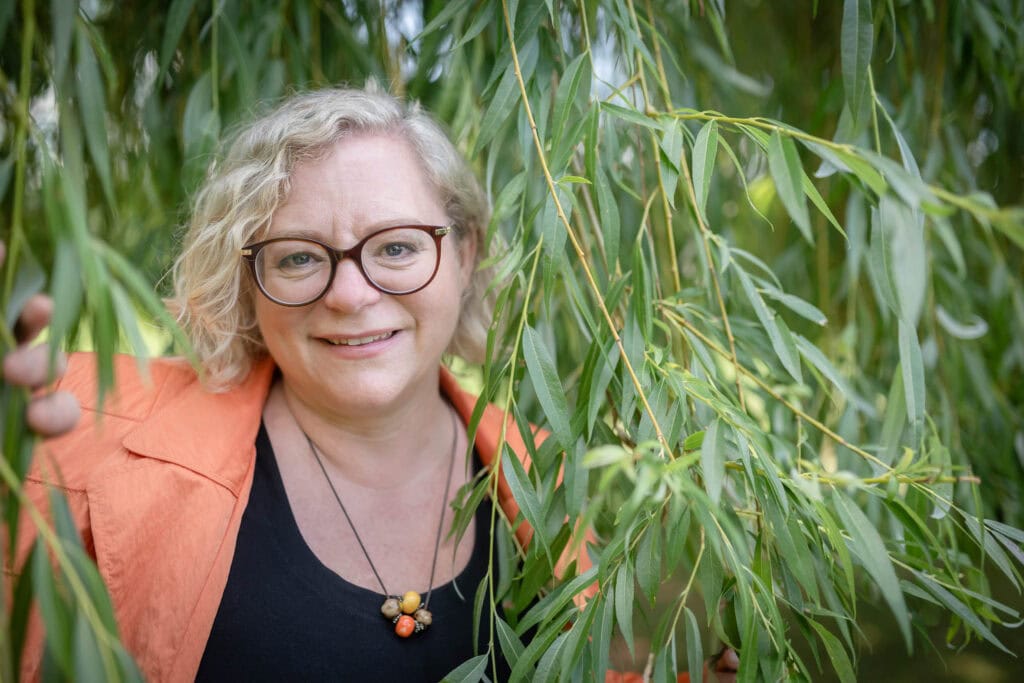 Freie Rednerin Sigrid Sudi inmitten von grünen Blättern, die für eine Veranstaltung in Österreich spricht.