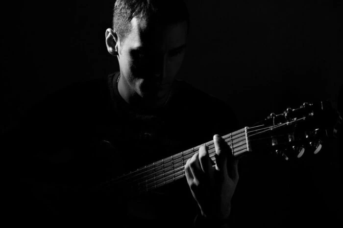 Junge Person spielt leise Gitarre bei einer Beerdigung, symbolisiert Abschied und Trost durch Musik.