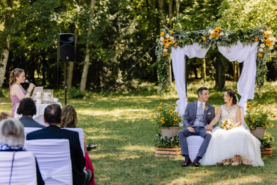Hochzeitspaar sitzt im Wald auf einer mit Blumen geschmückten Bank